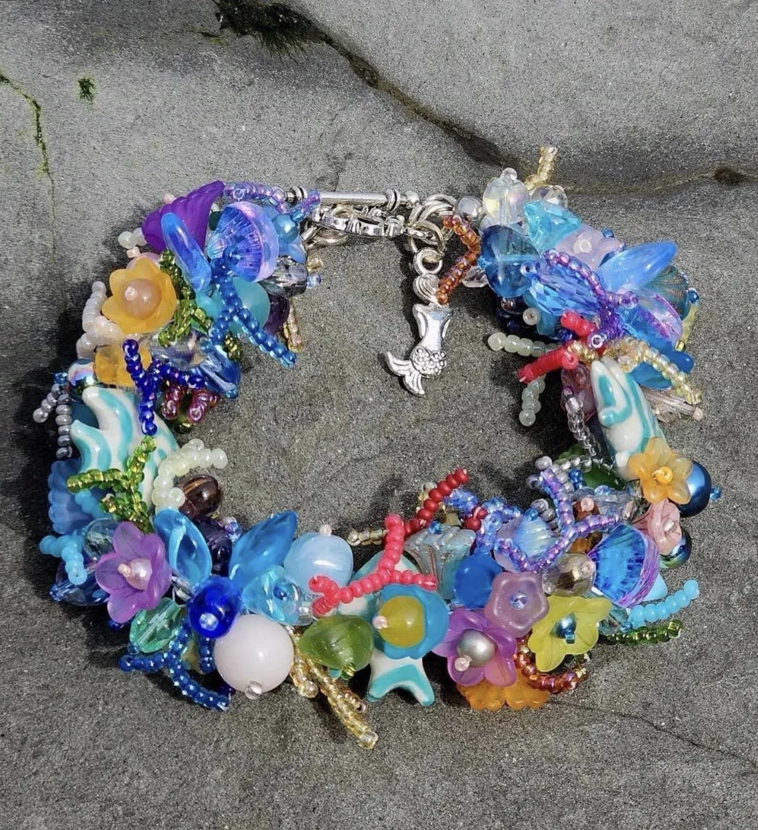 A blue ocean-themed beaded bracelet with a mermaid charm and coral beadwork on a grey stone