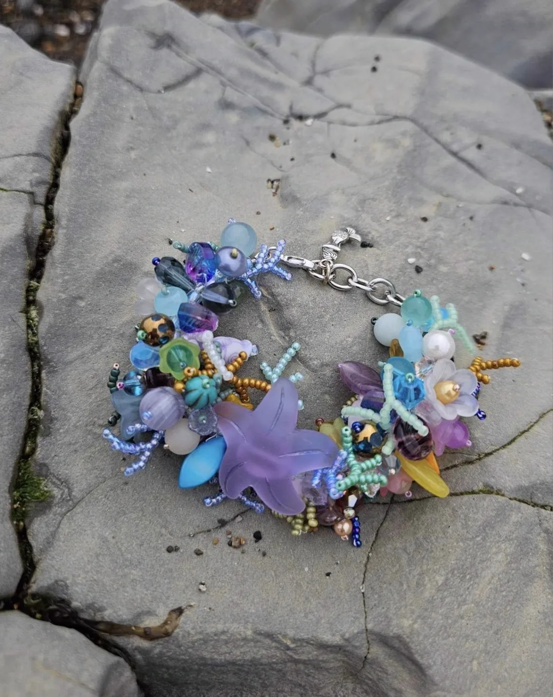 A light blue, lavender, and yellow beaded bracelet with a purple starfish centerpiece on a rock