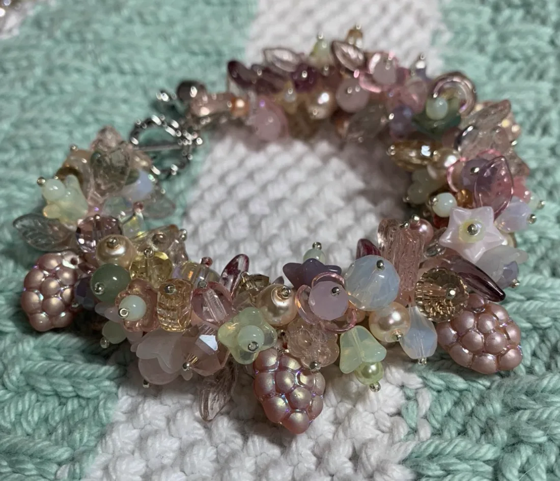 A pink, cream, and lavender beaded bracelet with raspberry beads and frosted glass flowers on knit fabric