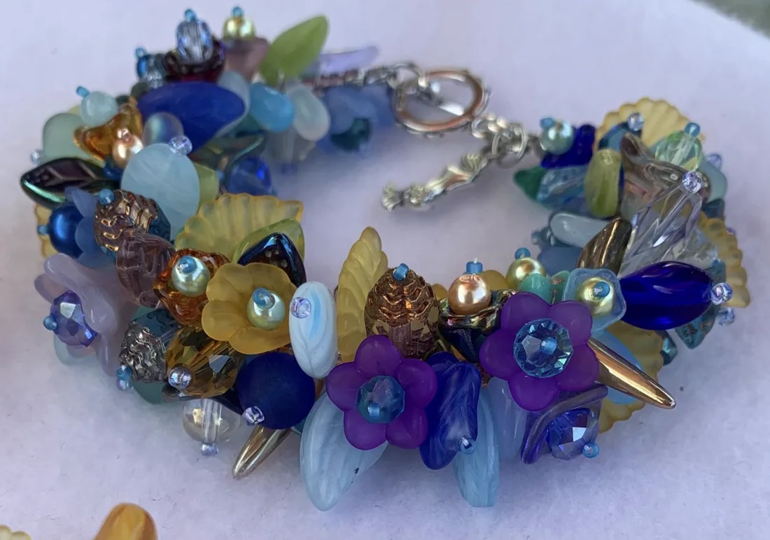 A cobalt blue, purple, and amber beaded bracelet with glass flowers, pearls, and a mermaid toggle clasp