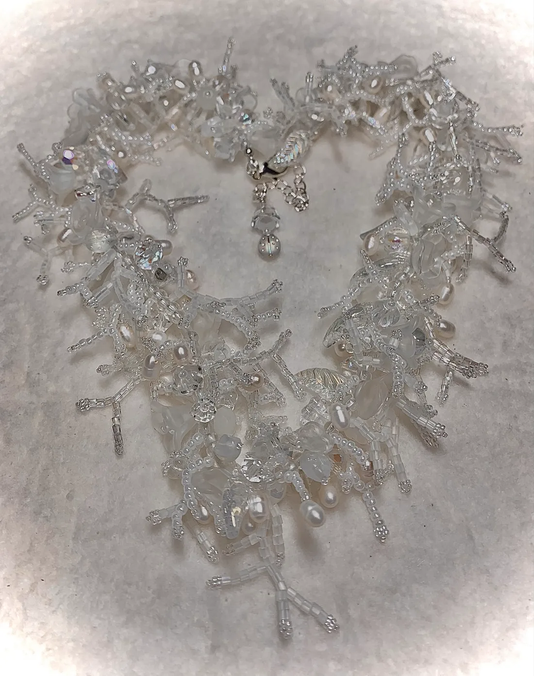 A white beaded fringe necklace laid out in a heart shape, coral-like texture