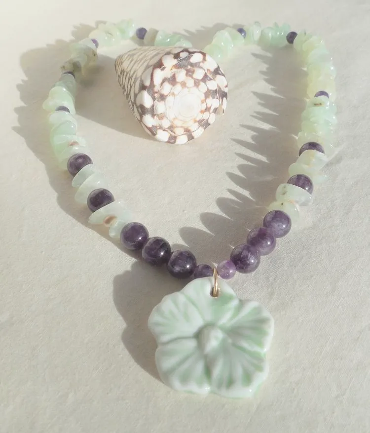 A beaded necklace with a pale green hibiscus flower pendant and a decorative seashell