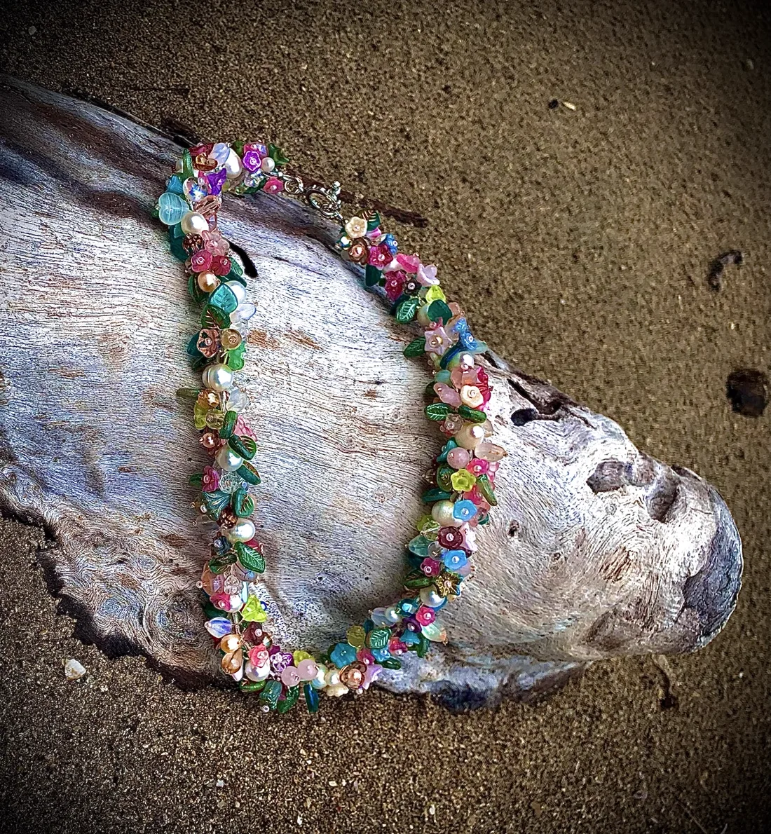 A colorful flower-themed beaded necklace draped over driftwood