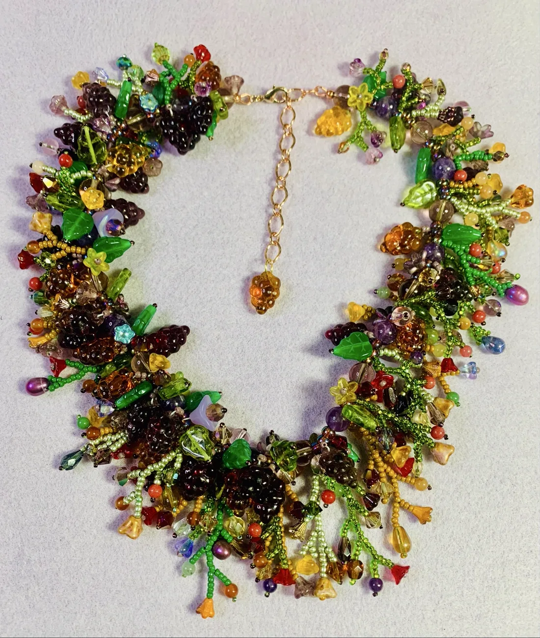 A cluster-style beaded necklace with three-dimensional grape, berry, and leaf clusters in purple, green, and amber