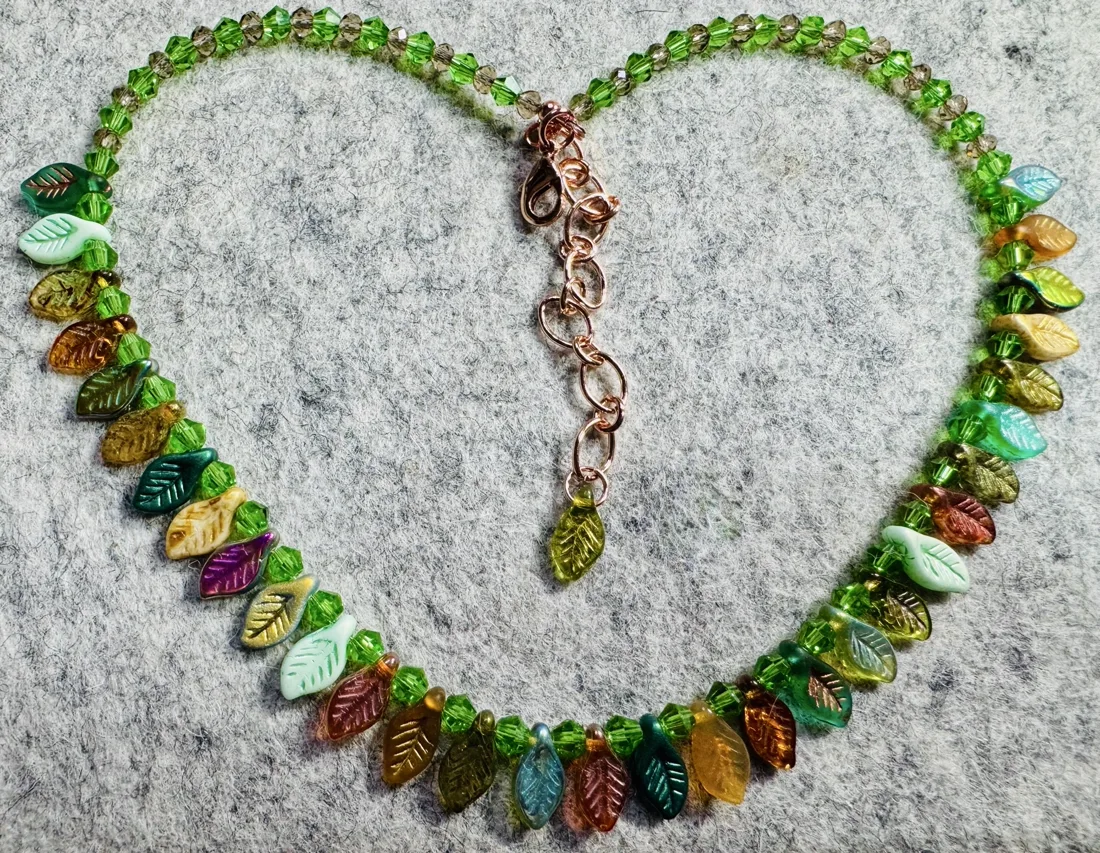 A leaf-themed beaded necklace with faceted bicone beads and glass leaf charms in autumnal colors