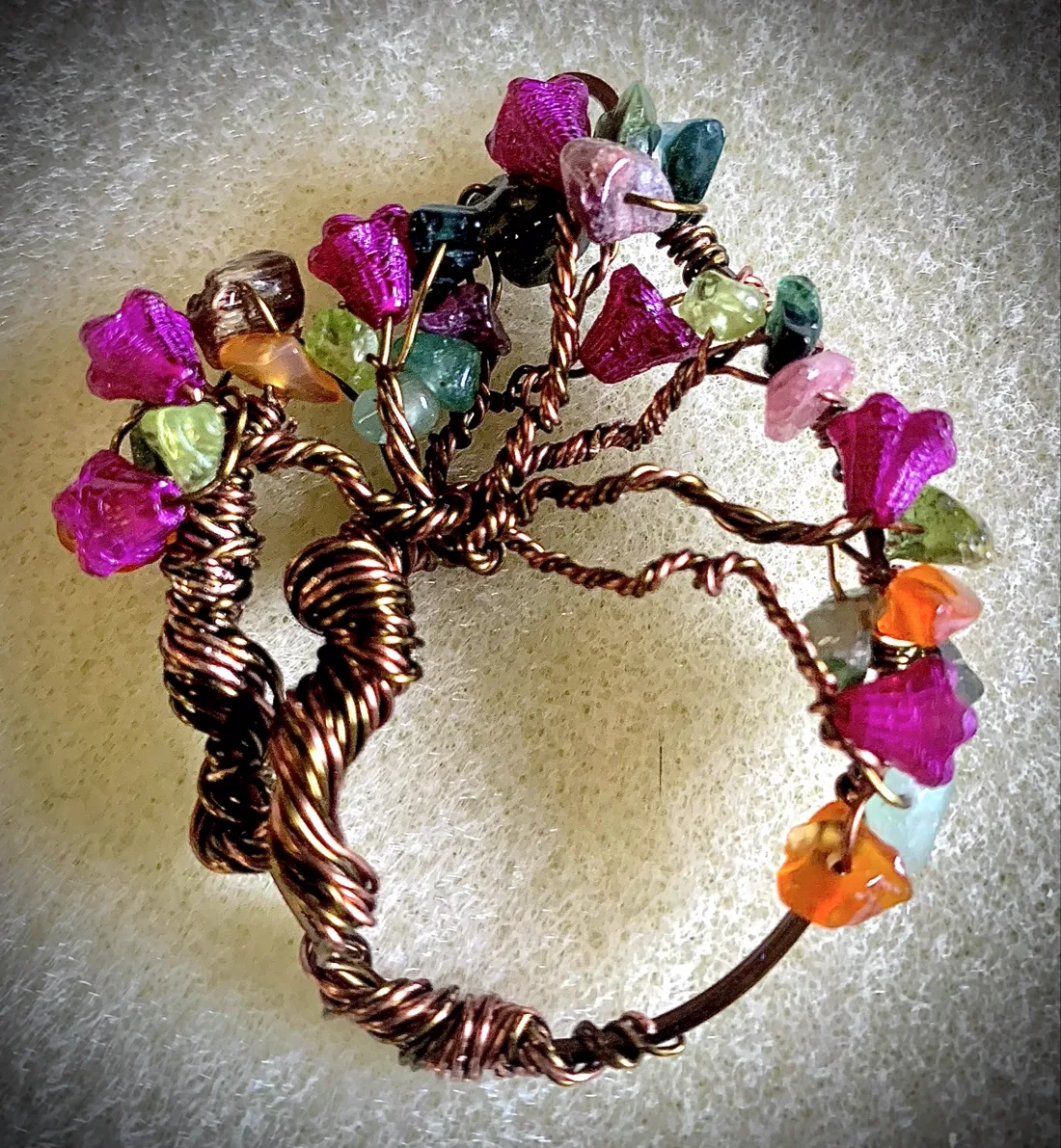 Close-up of a copper wire-wrapped tree of life pendant with magenta and green stone chips