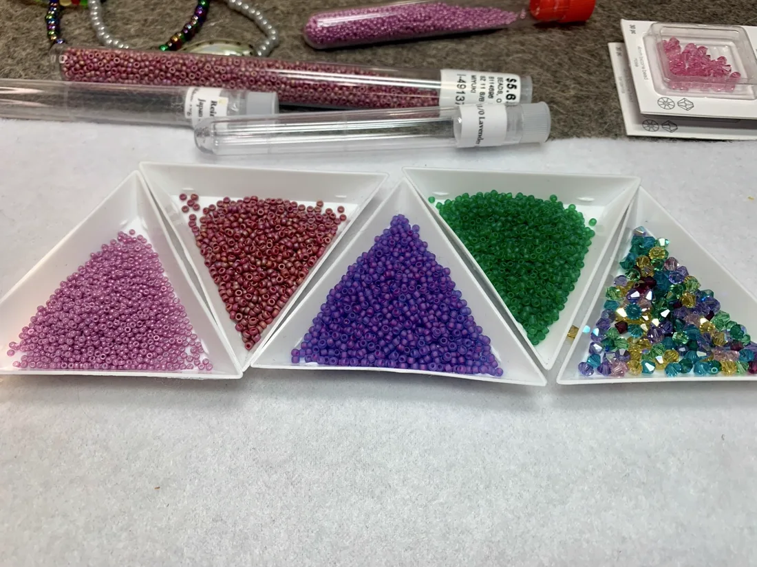 White trays filled with colored seed beads and tubes of beads with partially finished jewelry