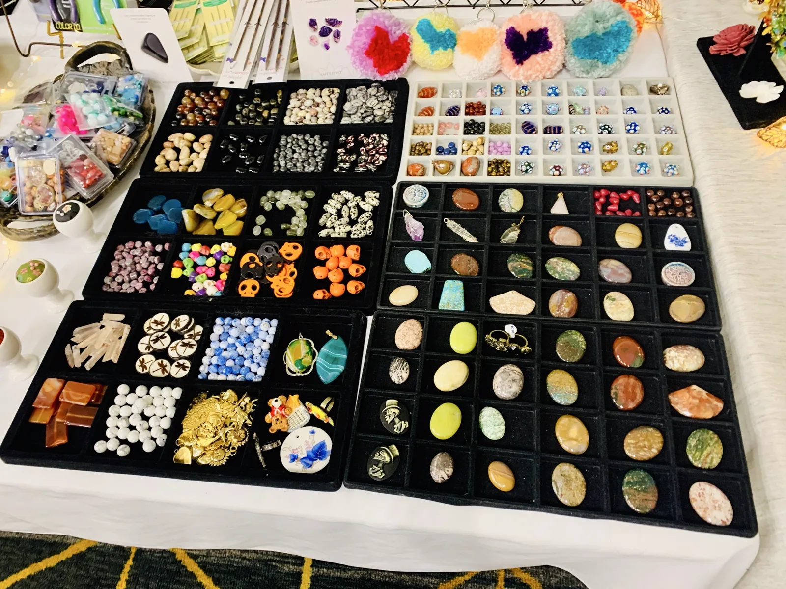 Overhead view of a worktable covered in bead trays, stone pendants, and jewelry findings